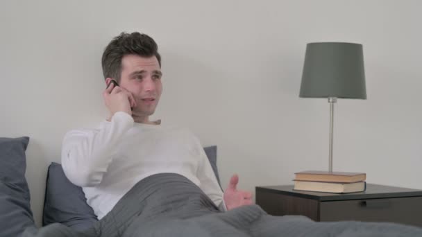 在床上用智能手机说话的愤怒男人 — 图库视频影像