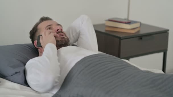 Hombre hablando de llamada en el teléfono inteligente en la cama — Vídeos de Stock