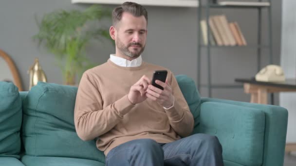 Mann som bruker smarttelefon i sofa – stockvideo