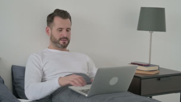 Hombre celebrando el éxito en el ordenador portátil en la cama — Vídeos de Stock