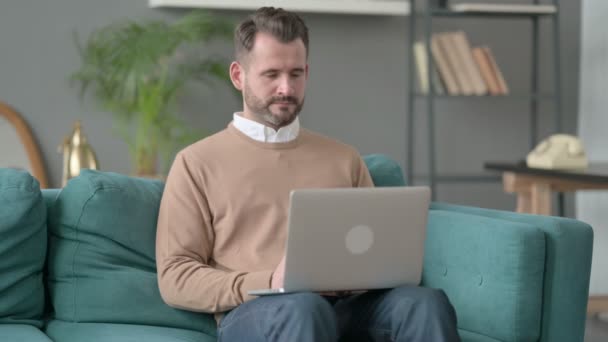 Человек плачет во время работы над ноутбуком на диване — стоковое видео