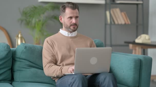 Человек с ноутбуком мыслит на диване — стоковое видео