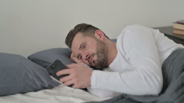 A férfi okostelefont használ, miközben alszik az ágyban — Stock videók