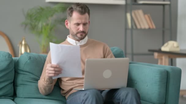 Muž s dokumenty pro čtení z notebooku na pohovce — Stock video