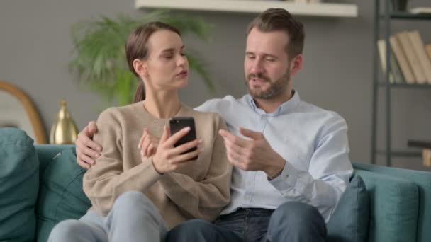 Portret pary przy użyciu smartfona podczas siedzenia na kanapie — Wideo stockowe
