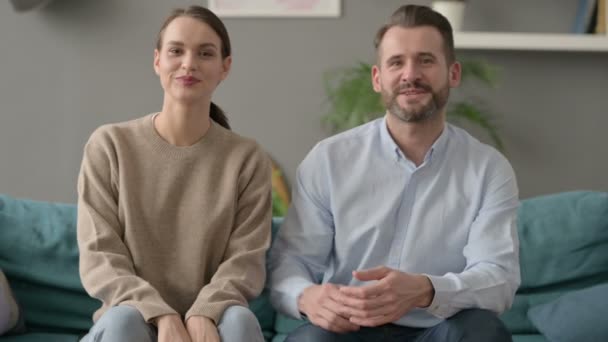 Casal sorrindo para a câmera enquanto sentado no sofá — Vídeo de Stock