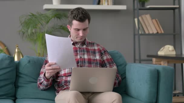 Homem com laptop trabalhando em documentos no sofá — Vídeo de Stock