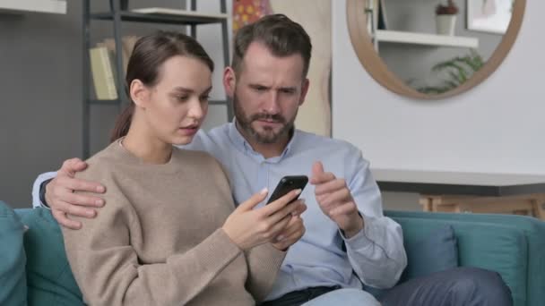 Portrait de couple réagissant à la perte sur Smartphone, assis sur le canapé — Video