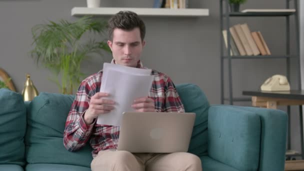 Man met laptop reageert op verlies op documenten, Sofa — Stockvideo