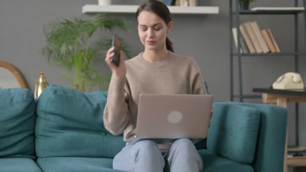 Mulher com laptop conversando no smartphone no sofá — Vídeo de Stock
