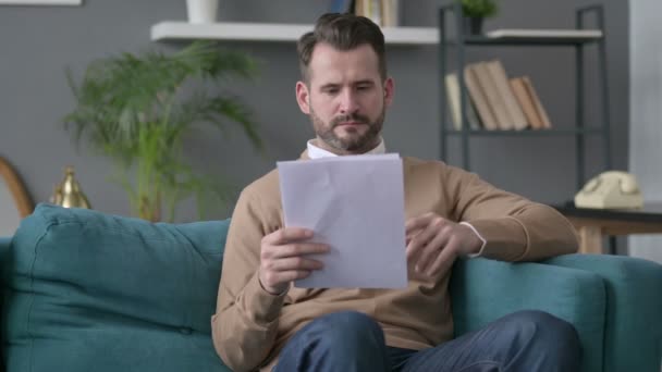 Mann liest Dokumente auf Sofa — Stockvideo