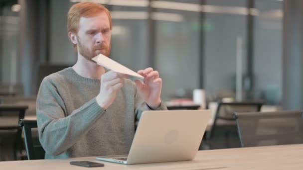 Скучный молодой человек делает бумажный самолет в офисе — стоковое видео