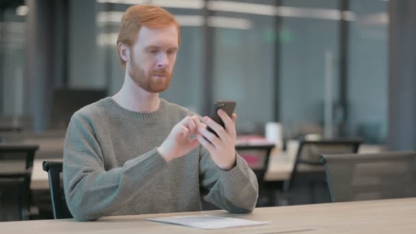 Houkutteleva nuori mies käyttää älypuhelinta toimistossa — kuvapankkivideo