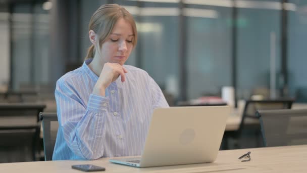Mujer joven pensando mientras trabaja en el ordenador portátil en la oficina — Vídeos de Stock