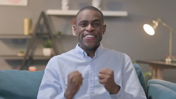 Porträtt av afrikansk man firar framgång medan du sitter på soffan — Stockvideo