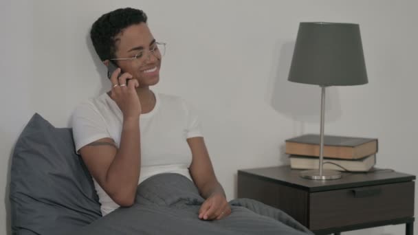 アフリカの女性がベッドの中でスマートフォンで通話中 — ストック動画