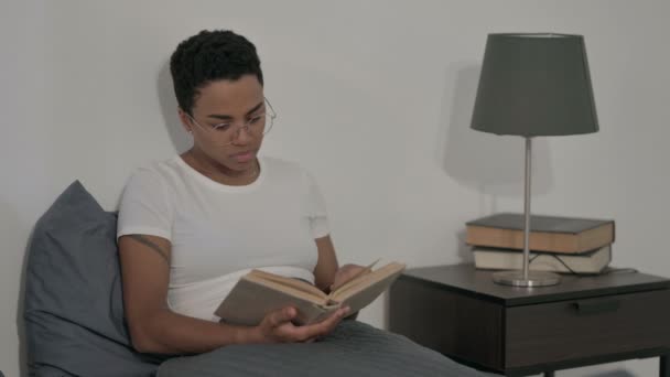 Afrikaanse vrouw die boek leest terwijl ze in bed zit — Stockvideo