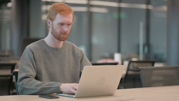 Молодой человек празднует успех во время использования ноутбука в офисе — стоковое видео
