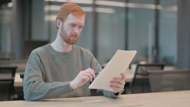 Молодой человек читает доклады во время работы в офисе — стоковое видео