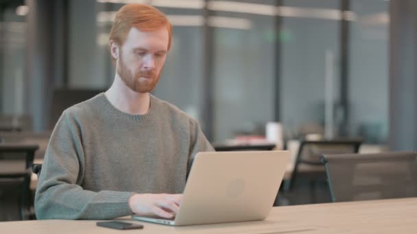 Молодой человек смотрит в камеру во время использования ноутбука в офисе — стоковое видео