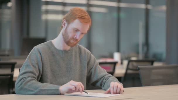 Молодой человек пишет на бумаге в офисе — стоковое видео