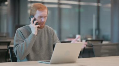 Ofiste dizüstü bilgisayar kullanırken Akıllı Telefonla Konuşan Kızgın Adam