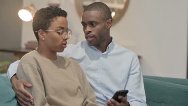 Retrato de casal reagindo à perda no smartphone, sentado no sofá — Vídeo de Stock