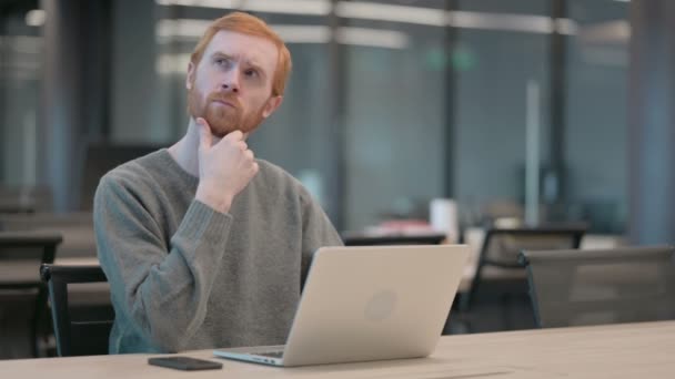 Молодой человек думает во время работы над ноутбуком в офисе — стоковое видео