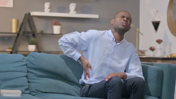 African Man mając ból pleców siedząc na kanapie — Wideo stockowe