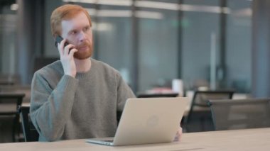 Ofiste dizüstü bilgisayar kullanırken Smartphone ile konuşan genç adam