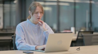 Ofiste dizüstü bilgisayar kullanırken boyun ağrısı çeken genç bir kadın. 