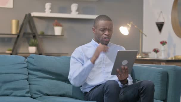 Afrikaanse Man reageert op verlies op tablet op bank — Stockvideo