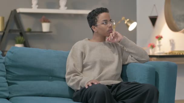 Mujer africana pensando mientras está sentada en un sofá — Vídeos de Stock