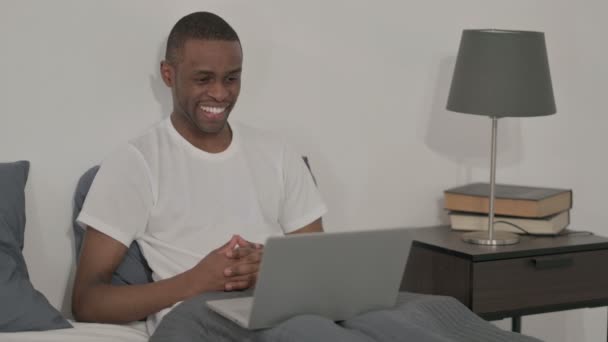 Africain faisant appel vidéo sur ordinateur portable au lit — Video