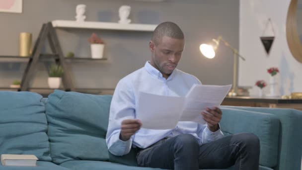 Hombre africano leyendo informes mientras está sentado en el sofá — Vídeos de Stock