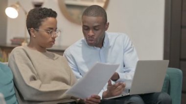 Çift, Sofa 'da dizüstü bilgisayarda çalışırken belgeler üzerinde tartışıyor 