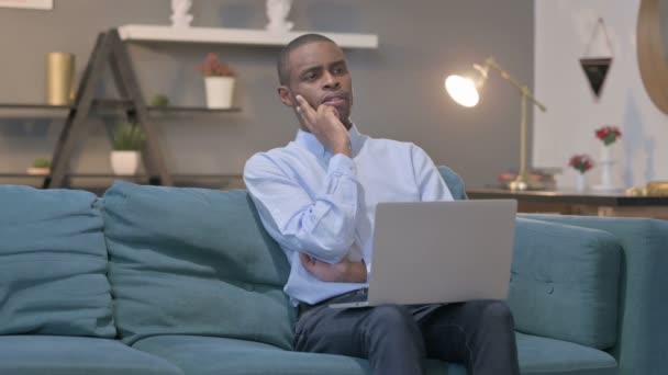 Hombre africano con portátil Pensando en el sofá — Vídeos de Stock