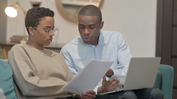 Casal discutindo sobre documentos enquanto trabalhava laptop, no sofá — Vídeo de Stock
