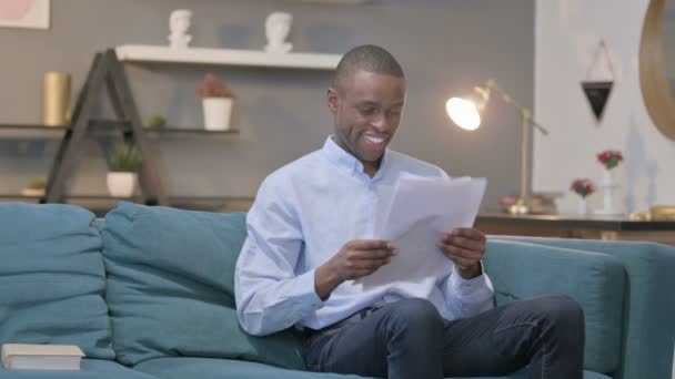 Hombre africano molesto mientras lee documentos en el sofá — Vídeos de Stock