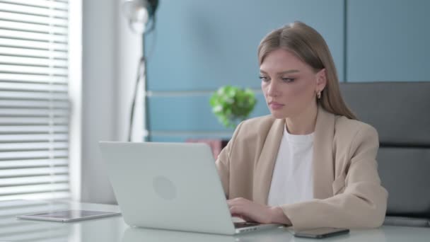 Mujer de negocios mirando a la cámara mientras usa el ordenador portátil en la oficina — Vídeo de stock