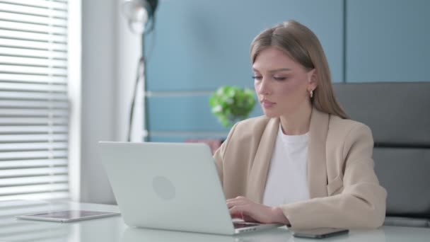 Mujer de negocios señalando a la cámara mientras usa el ordenador portátil en la oficina — Vídeos de Stock