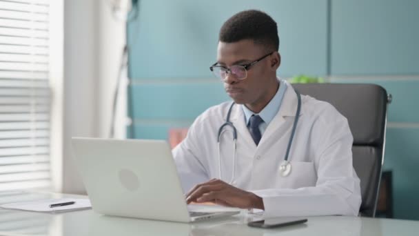 Junger afrikanischer Arzt blickt im Büro mit Laptop auf Kamera
