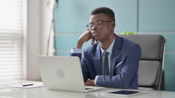 Joven empresario africano tomando siesta mientras está sentado en la oficina con el ordenador portátil — Vídeo de stock