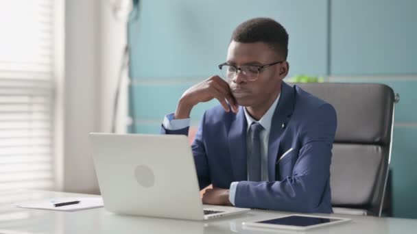 Νεαρός αφρικανός επιχειρηματίας σκέφτεται ενώ εργάζεται σε φορητό υπολογιστή στο γραφείο — Αρχείο Βίντεο