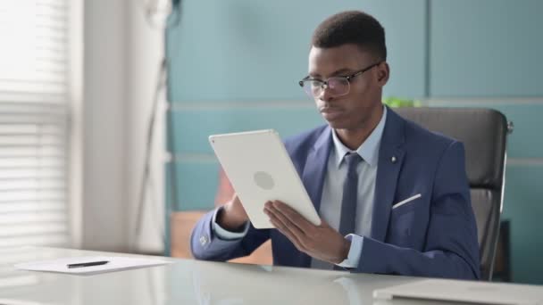 Молодой африканский бизнесмен, сидя в офисе, пользуется планшетом — стоковое видео