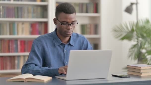 Jonge Afrikaanse man glimlachen bij de camera tijdens het gebruik van laptop — Stockvideo