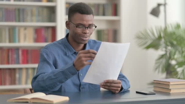 事務所で書類を読みながら成功を祝う若いアフリカ人男性 — ストック動画