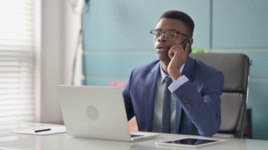 Ofiste dizüstü bilgisayar kullanırken telefonda konuşan genç Afrikalı İşadamı