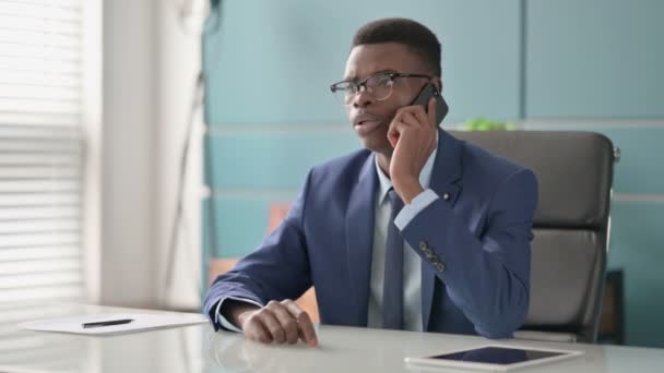 Rozzlobený mladý africký podnikatel mluví na telefonu v kanceláři — Stock video