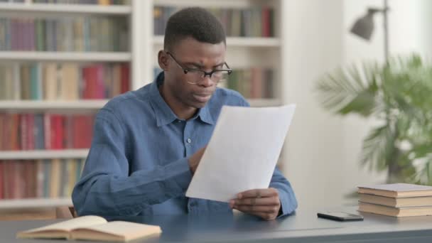 事務所に座っている間に若いアフリカ人男性の読書レポート — ストック動画
